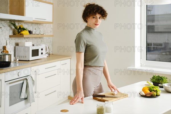Woman stands in a well-lit modern kitchen preparing ingredients on a table. Young woman is ready to cook healthy food