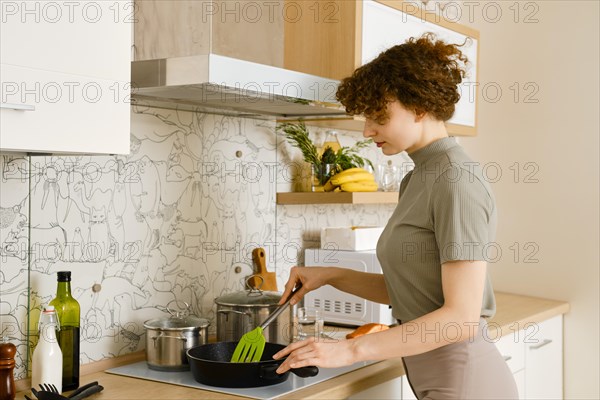 Young housewife stirring food in a frying pan while preparing healthy meal