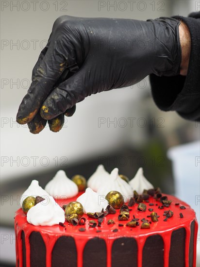 A professional pastry chef wear black gloves artfully decorating a chocolate cake with golden painted chocolate sprinkles on the top