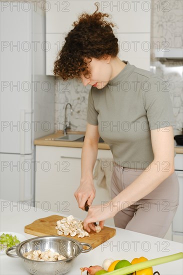 A housewife cutting fresh champignon in the kitchen on wooden cutting board