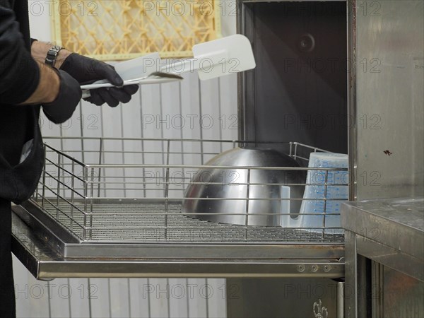 Chef's hand holding a spatula over a dish washer in a professional kitchen setting