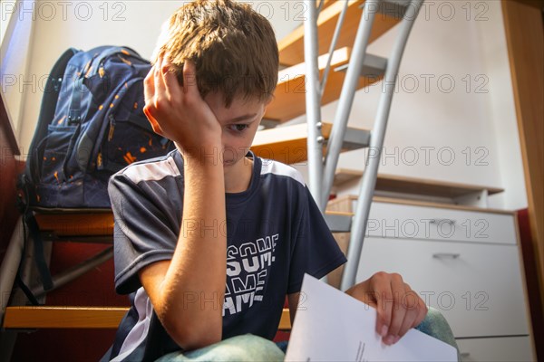 Sad pupil sitting on a staircase with his report card in his hand (symbolic image)