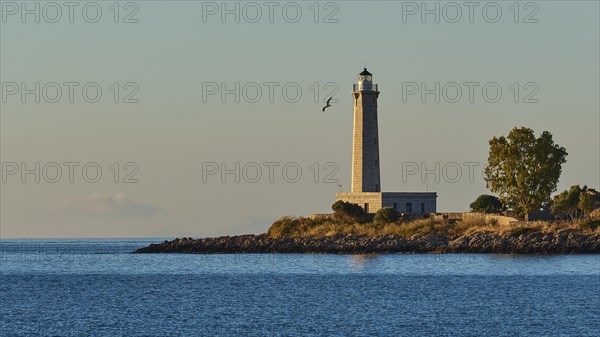 Lighthouse on the coast at dusk with a flying bird in the background, Gythio, Mani, Peloponnese, Greece, Europe