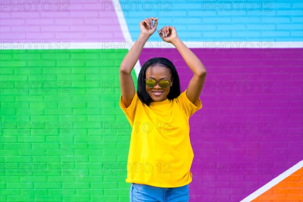 Frontal portrait of an african woman with sunglasses dancing next to multicolored wall