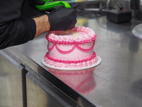 Decorating with text mesagge the top of pink cake with intricate icing patterns using a pastry filling bag