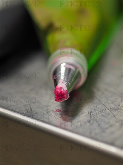 Close-up of a piping pastry bag tip with a bit of pink icing on it, resting on a metal surface