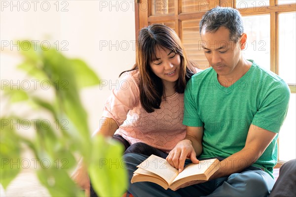 Two Asian adults reading a book, sharing a moment of study and knowledge. Two Japanese male and female students reading a book. Young asian couple reading a book at home