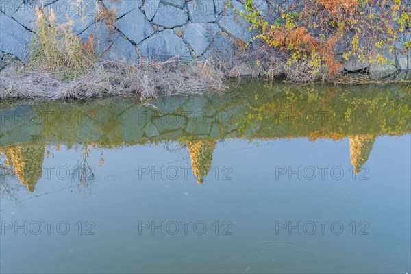 Three Rock cairn on edge of canal reflected in calm blue water in South Korea