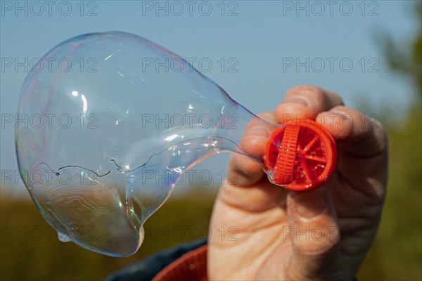 Soap bubble blowing ring with coloured film of soapy water in front of a blue sky