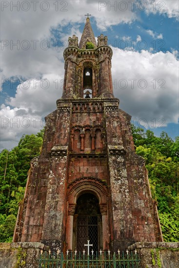Close-up of an old Gothic church tower of Capela de Nossa Senhora das Vitorias with a cross against a cloudy sky, Terra Nostra Park, Furnas, Sao Miguel, Azores, Portugal, Europe