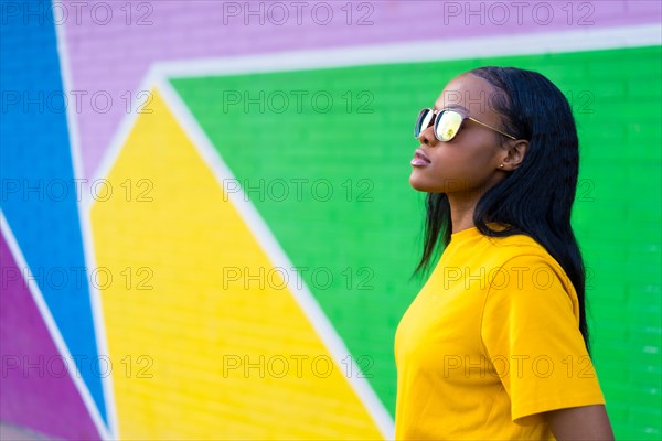 Side view of a serious cool african woman with sunglasses next to a colorful wall