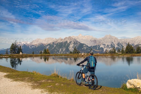 Mountain biker taking a break at the Kaltwassersee lake in Seefeld/Tyrol. The snow-covered peak on the left of the picture is the Zugspitze