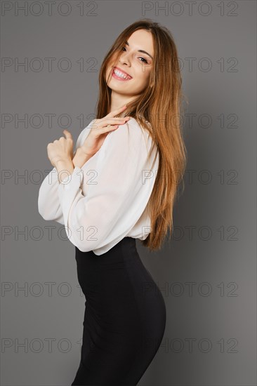 Smiling woman in pencil skirt and blouse standing in profile on grey background
