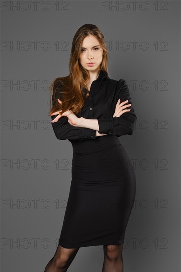 Serious young woman in black blouse and skirt with folded arms