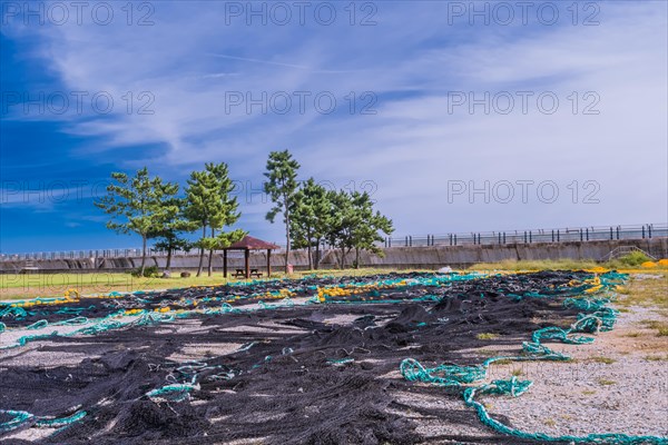 Large fishing nets laid out to dry in gravel lot in front of sea wall and next to public park on cloudy day in South Korea