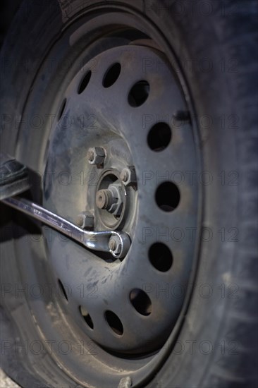 Vertical detail of an unrecognizable mechanic loosening lug nuts to change a flat tire on a vehicle