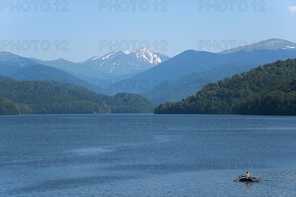 A small boat on a calm blue reservoir with snow-capped mountains in the background, Vidraru Reservoir, Transfogarasan High Road, Transfagarasan, TransfagaraÈ™an, FagaraÈ™ Mountains, Fagaras, Transylvania, Transylvania, Transylvania, Ardeal, Transilvania, Carpathians, Romania, Europe