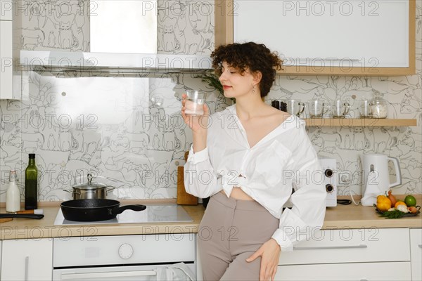 Young woman standing in profile in the kitchen with glass of pure water