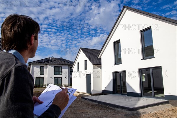 Symbolic image of an architect or builder: man with a building plan in front of a detached house