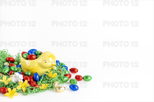 Chocolate eggs and a decorative chick surrounded by artificial grass as a festive decoration, white background