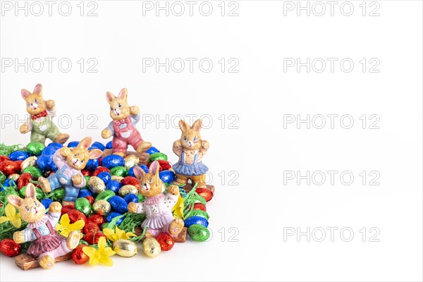 Several Easter bunny figures surrounded by colourful chocolate eggs on artificial grass, white background