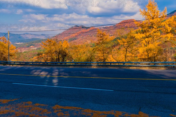 Mountains with trees in fall colors under low level clouds from side of three lane mountain road in South Korea