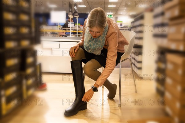 Elegant young woman trying on knee-high black boots in a shop
