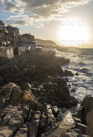 Sea water crashes against the cliffs of the rugged coastline in the town of Cefalu, Sicily, Italy, Europe