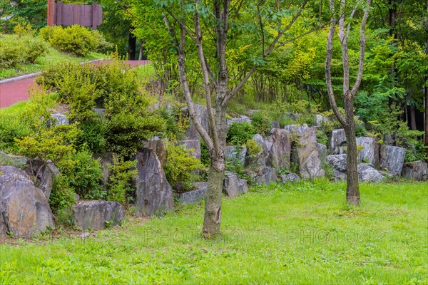 Wall of large boulders in lush urban public park with walking path going uphill in background in South Korea