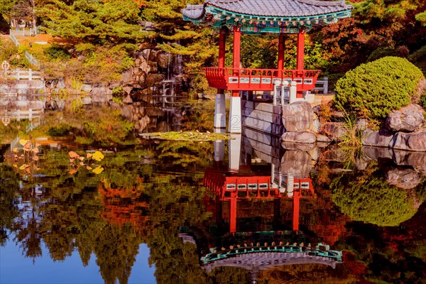 Beautiful oriental gazebo with terracotta tile roof at edge of man made pond with small waterfall in background in South Korea