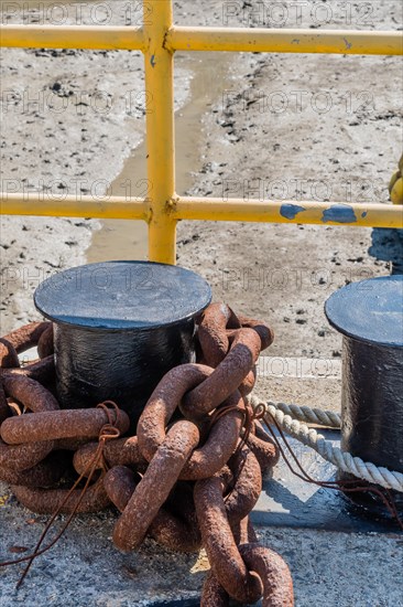 Rusty chain wrapped around ships mooring post in front of yellow metal fence in Yeosu, South Korea, Asia