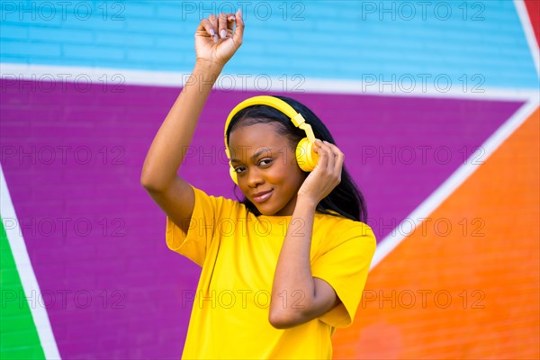 Sensual african woman looking at camera while dancing listening to music against a colorful wall