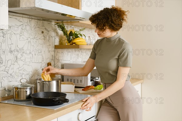 Housewife adds pappardelle pasta into pot with boiling water in bright kitchen