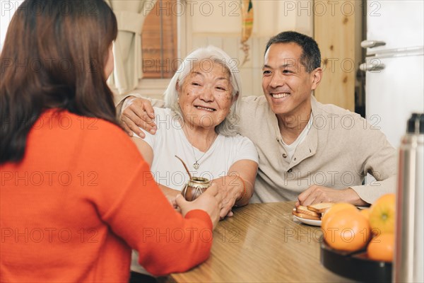 Happy adult children sharing with their elderly Japanese mother drinking mate in the kitchen. Argentine-Japanese family