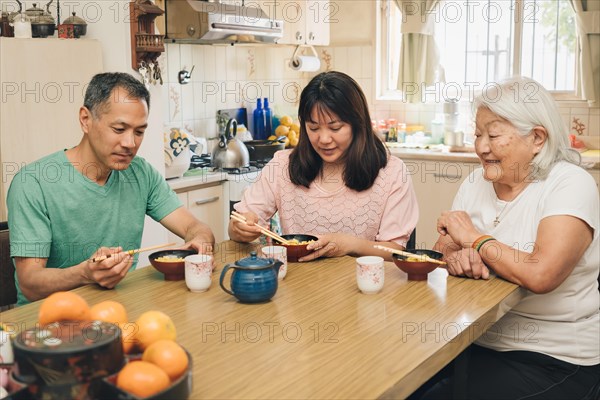 Japanese adult family eating rice with chopsticks. White-haired elderly mother enjoys watching her grown children sharing Japanese typical lunch