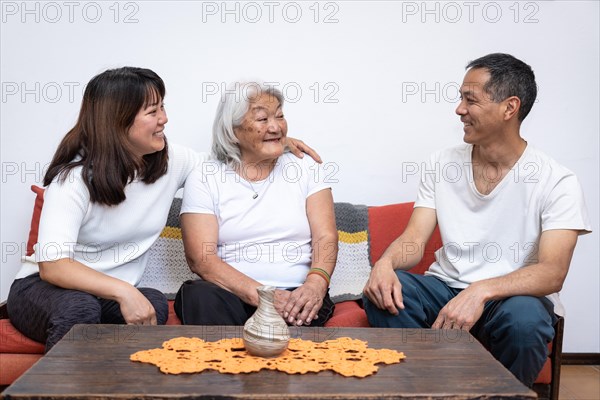 Adult children visit their mother of Japanese origin, chatting amicably sitting on sofa