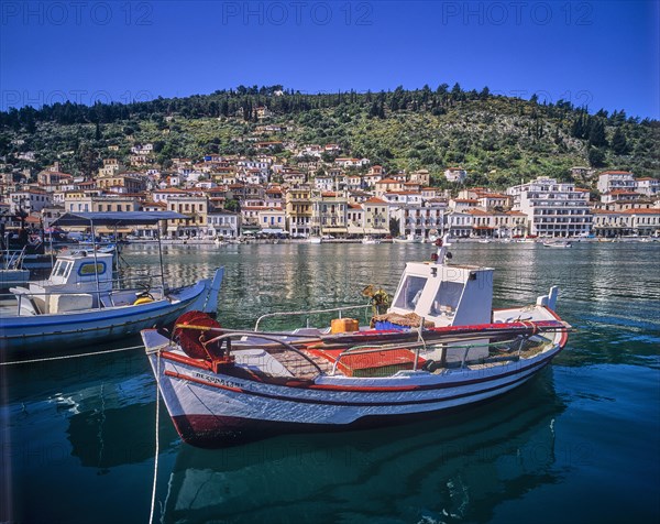 Small boats in the calm harbour water with mountain and city view in the background, Gythio, Mani, Peloponnese, Greece, Europe