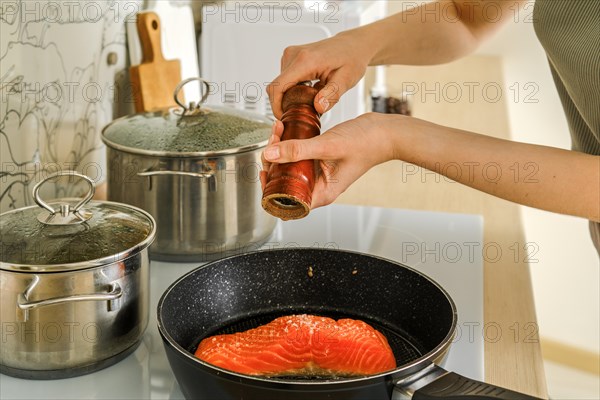 Female hands sprinkle trout fillet with pepper from a wooden hand mill