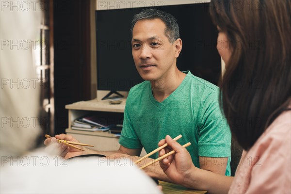 Japanese man eating at home with chopsticks looks and smiles at his family