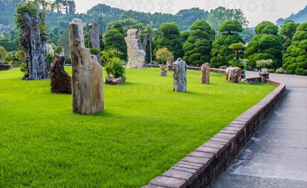 Rock garden of petrified wood and stalactites next to paved walkway in manicured park in South Korea