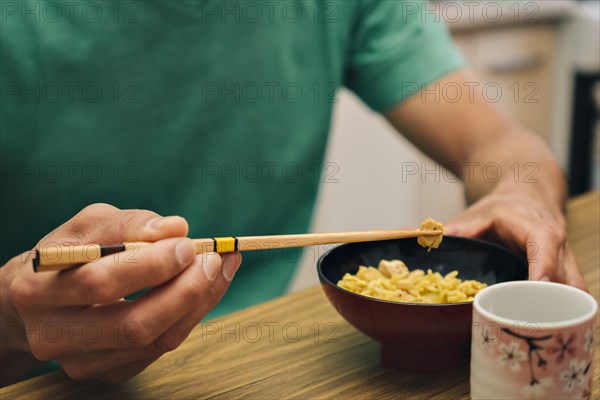 Close-up detail of male hands holding chopsticks eating rice from a bowl. Concept of traditional Asian