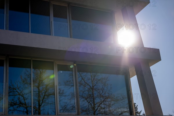 Modern Design Building with Tree Reflection and Against Clear Blue Sky and Sunlight with Lens Flare in a Sunny Day in Switzerland