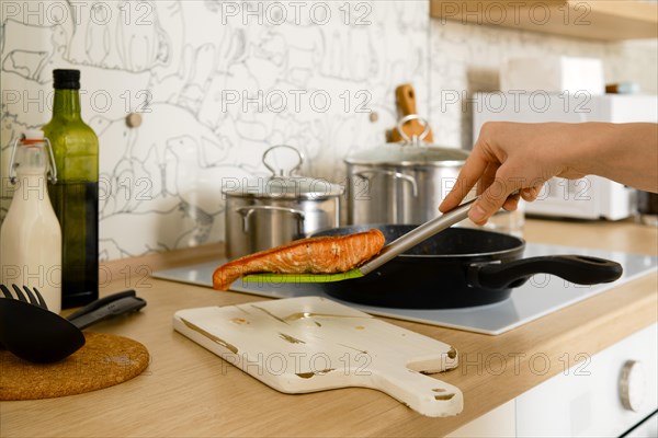 Closeup view of female hand holding fried trout steak on a spatula over the serving board in the kitchen