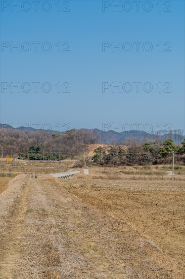 Landscape of dry farmland with concrete drainage aqueduct in distance under clear blue sky