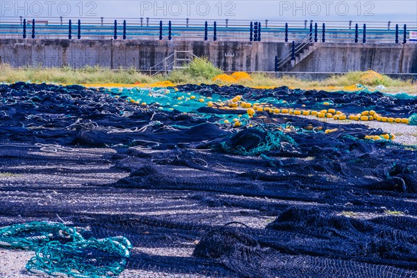 Large fishing nets laid out to dry in gravel lot in front of sea wall on cloudy day in South Korea