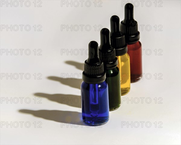 Four glass eye dropper bottles filled with blue, green, yellow and red liquid casting dark shadows on white background