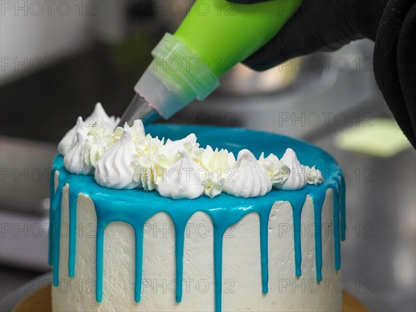 Decorating a cake with white icing using a pastry bag, with blue frosting dripping