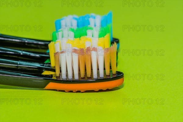 Closeup of four toothbrushes in orange, yellow, green and blue on a green background