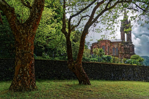 Hidden Gothic church Capela de Nossa Senhora das Vitorias behind trees and an old stone wall in a quiet green area, Furnas Lake, Furnas, Sao Miguel, Azores, Portugal, Europe