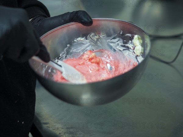 Pastry chef wearing black gloves for hygiene Stirring pink frosting in a steel bowl with a white spatula